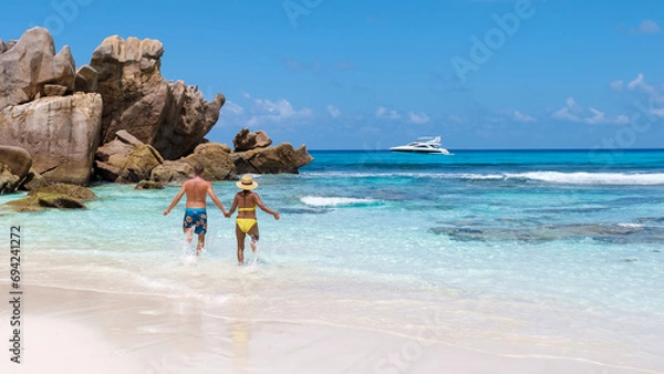 Fototapeta Anse Cocos Beach La Digue Island Seychelles, a happy couple of men and woman walking at the beach at a luxury vacation in the Seychelles, men and woman jumping in sky happiness on vacation 