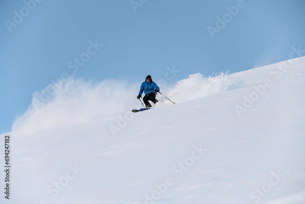 Fototapeta Skier with poles in his hands goes down a snowy slope