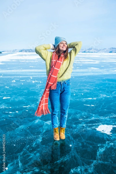 Obraz Happy smiling female traveler enjoying good day while standing on frozen Baikal lake with beautiful cracked ice floes inside