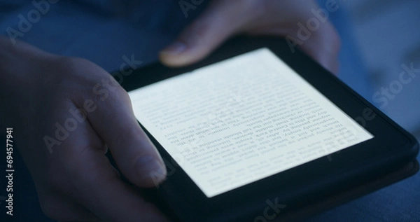 Fototapeta A woman reading an e-book in the evening or by night