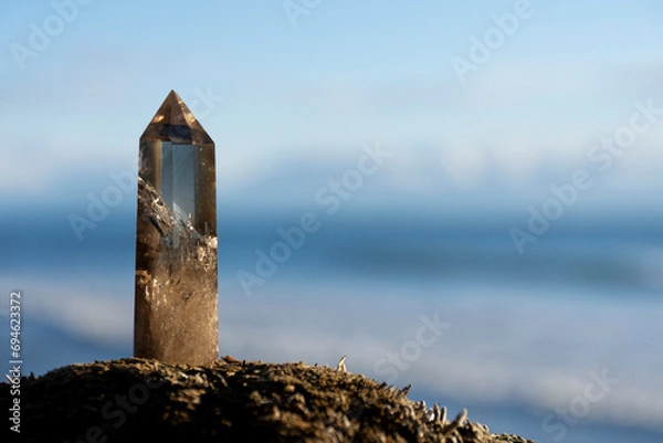 Fototapeta A close up image of a healing smoky quartz crystal tower with the blue Pacific Ocean in the background. 