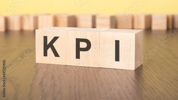 Fototapeta three wooden cubes on a yellow background, with the abbreviation KPI - Key Performance Indicators