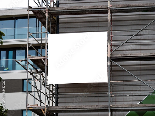 Fototapeta Empty banner on a construction site template. White copy space for a company logo or information of the building. The advertisement is mounted to the scaffolding on the exterior.