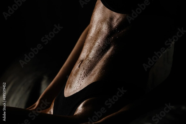 Fototapeta athletic figure without underwear of a sexy girl belly with drops of sweat and water in the gym in a low key	