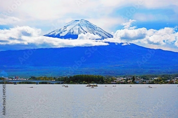 Fototapeta Fujiyama mountain before the lake with trees, houses, buildings, bridge, and ships under cloudy-blue sky background 