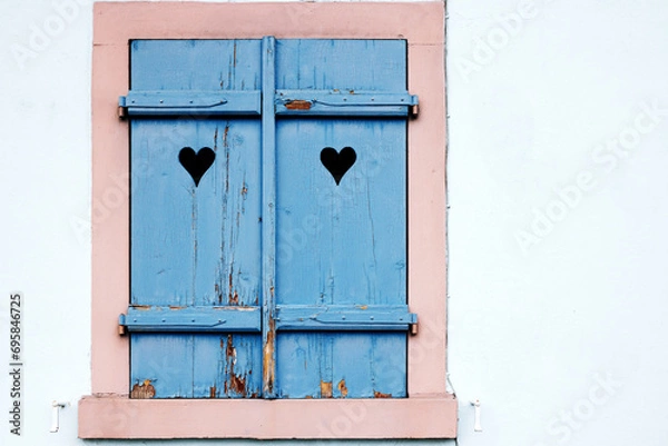 Fototapeta The closed window shutter is blue with cracked paint and a symmetrical pattern
