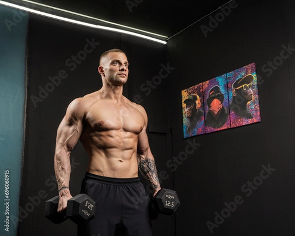 Obraz A man with a beautiful athletic body holds dumbbells in his hands and looks away