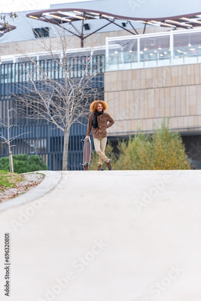 Obraz Young skateboarder with stand-up skateboard on an urban road, with modern buildings in the background and a relaxed atmosphere