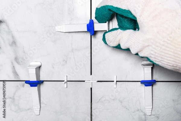 Fototapeta Tiler's hand installing leveling system tiles.