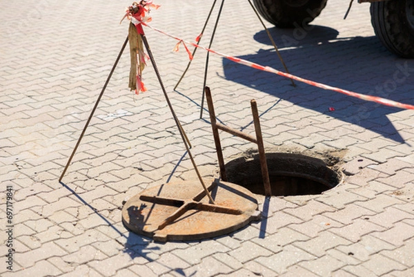 Fototapeta An open sewer hatch during technical work. Background with selective focus and copy space