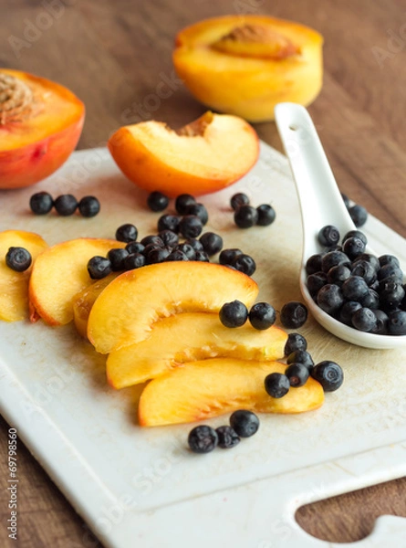 Fototapeta peach slices and blueberries in spoon on a white board