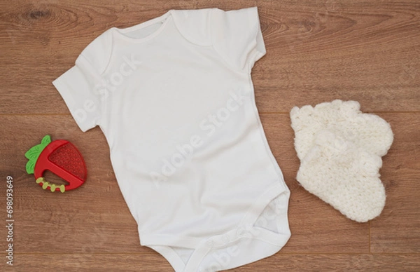 Fototapeta Mockup of white baby bodysuit on wood background with knitted booties. Blank baby clothes template mock up. Flat lay styled stock photo.