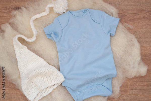 Fototapeta Mockup of blue baby bodysuit on wood background with knitted hat. Blank baby clothes template mock up. Flat lay styled stock photo.