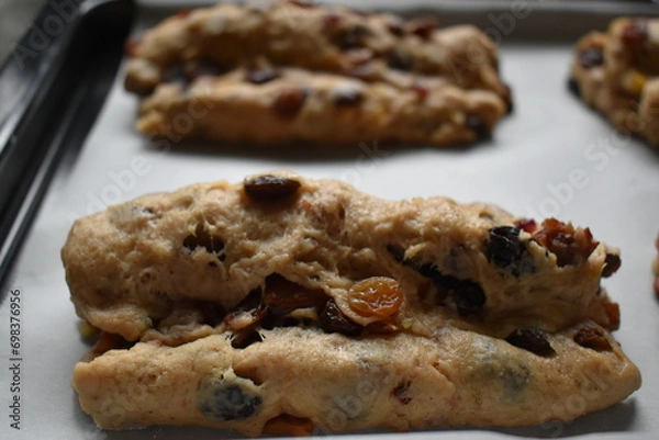 Fototapeta Bread dough with dried fruit mix on a baking tray. Stollen shape.