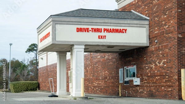 Obraz Drive-thru pharmacy exit with red signage on a brick building, covered drive-up window, and a clear day.