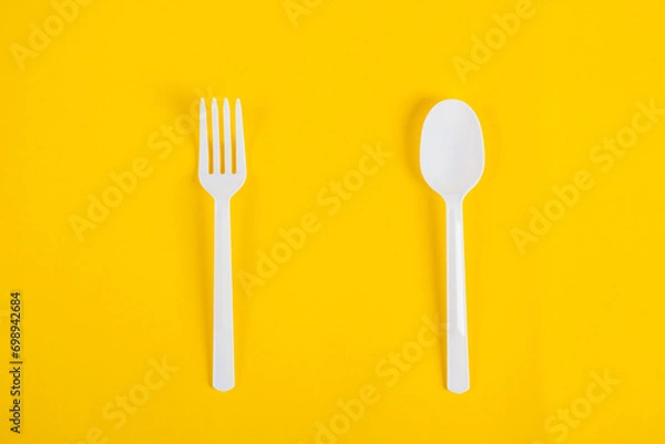 Fototapeta White plastic spoon and fork isolated on yellow background