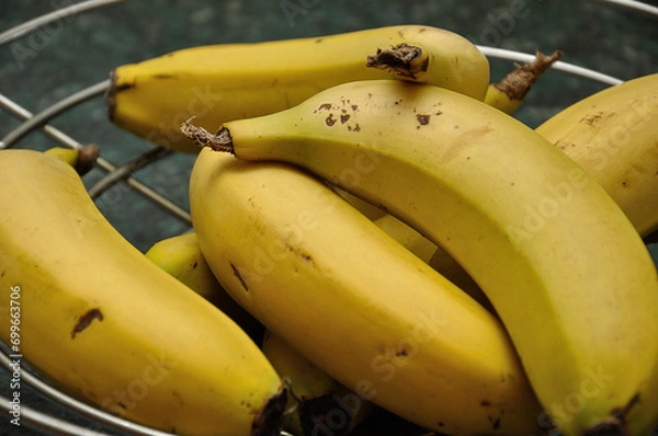 Obraz A bunch of bananas in a wire fruit basket