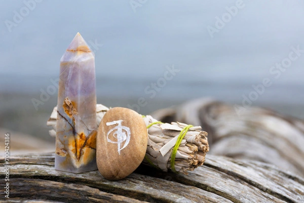 Fototapeta An image of a healing reiki symbol with white sage smudge stick and crystal tower on an old weathered driftwood log. 