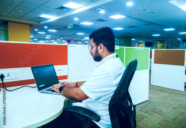 Fototapeta Bangalore, India- 15th October 2023:Young Indian employee working using laptop at his desk in a modern office.