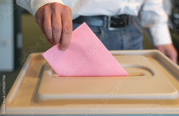 Fototapeta Stimmabgabe im Wahlbüro: Nahaufnahme der Hand eines Mannes, der seinen Stimmzettel in die Wahlurne steckt, viel Copy Space