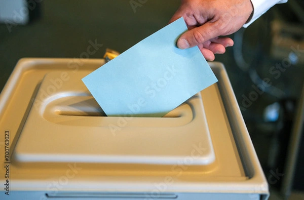 Fototapeta Stimmabgabe im Wahlbüro: Nahaufnahme der Hand eines Mannes, der seinen Stimmzettel in die Wahlurne steckt, viel Copy Space