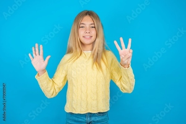 Fototapeta Beautiful kid girl wearing yellow sweater holding notebook showing and pointing up with fingers number eight while smiling confident and happy.