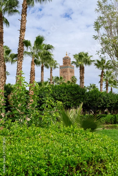 Obraz Photo of the upper part of the tower of the Koutoubia mosque in the city of Marrakech, tower covered by trees and palm trees. Cloudy day.