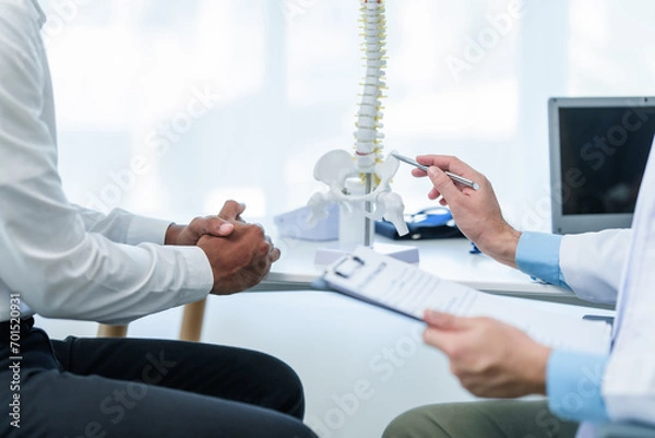 Fototapeta Close up male doctor and patient people in a medical office, spine model, possibly discussing spinal condition or syndrome with the patient.