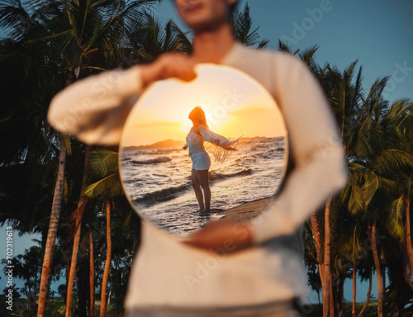Fototapeta Man holding a mirror in his hand The reflection is a woman standing on the beach.