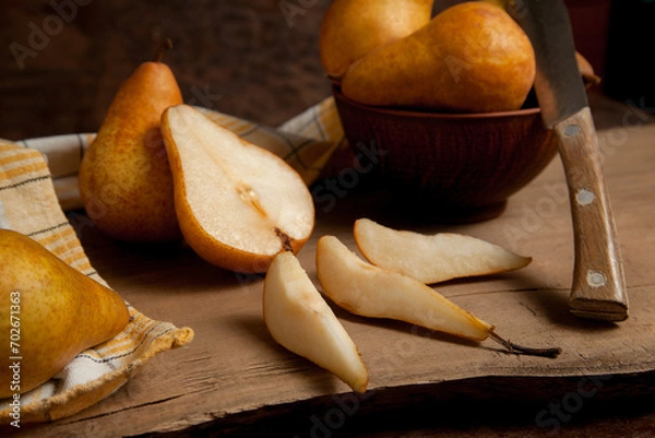 Obraz Whole, half and slices of pears and bowl with fruits on wooden background with yellow kitchen towel..