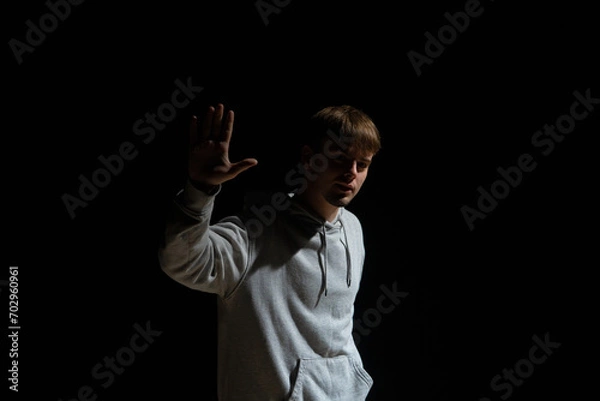 Fototapeta Guy in light street clothes poses on black background of studio. Dancer demonstrates elements of choreography in hip hop style. Modern street dance style.
