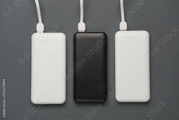Fototapeta Power banks with cable on dark gray background. External batteries for charging smartphone and other gadgets. Top view