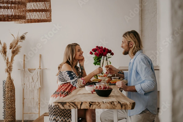Obraz Joyful young loving couple toasting with champagne while having romantic dinner at boho style home