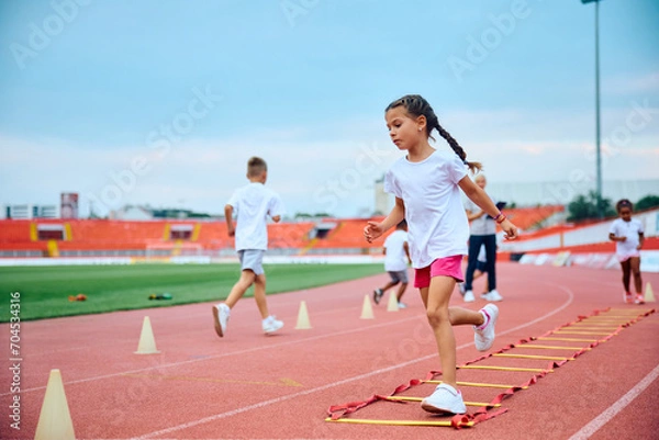 Fototapeta Little girl having PE class on running track at stadium.