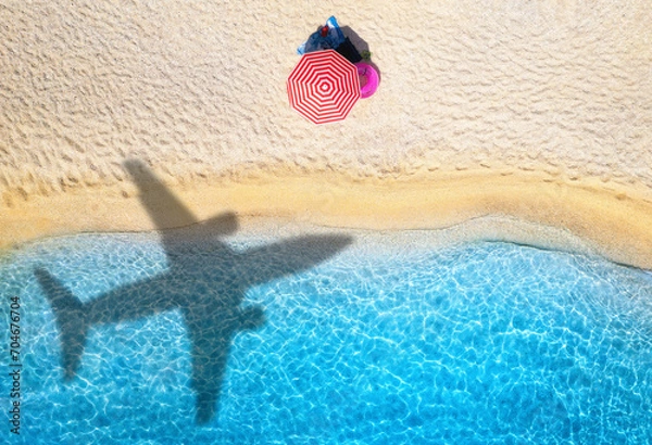 Fototapeta Aerial view of blue sea, airplane shadow, empty sandy beach with umbrella at sunset in summer. Tropical landscape with blue water, shadow of flying plane. Travel and vacation in islands. Top view