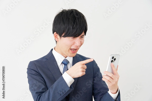 Fototapeta スマートフォンを見て怒るビジネスマン　白背景