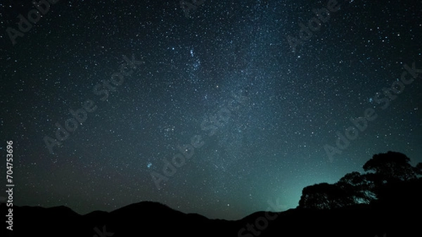 Fototapeta Dark starry night sky in the wilderness with a silhouette of mountains and trees in the background.