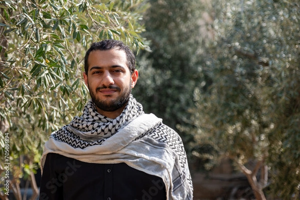 Fototapeta portrait for male wearing keffiyeh in olive tree field with black background and black shirts also with smile facial expression