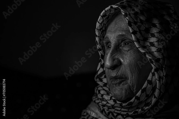 Fototapeta portrait of an old lady in dark background wearing white palestinian keffiyeh with smile on her face looking for freedom and hope to Right of Return for Palestinians