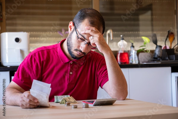 Fototapeta man sitting in the kitchen and calculating the costs of living feeling frustrated