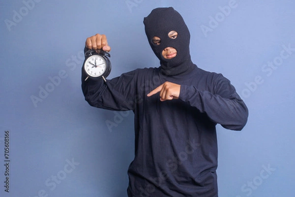 Fototapeta Angry man in black mask pointing with finger at alarm clock