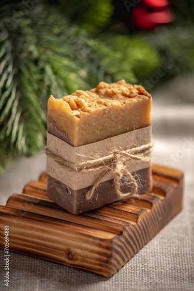Fototapeta Fragrant yellow brown piece of natural soap on an organic wooden soap dish against the background of the green branches of a coniferous tree