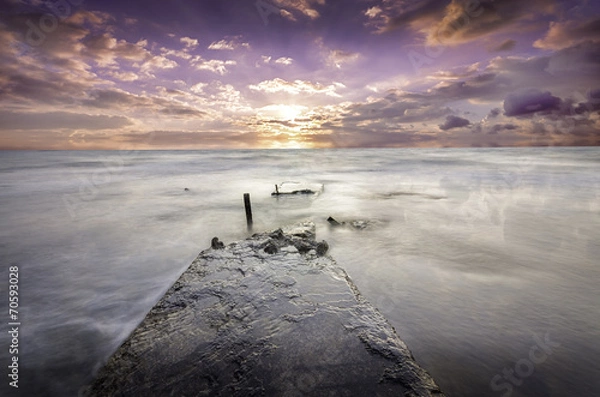 Fototapeta lonely destroyed pier extending deep into the ocean at sunset