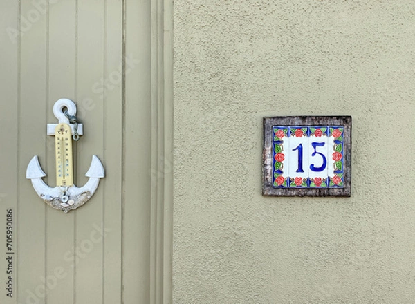 Fototapeta Fifteen. Number fifteen on a wall and an anchor-shaped external thermometer. Address made with ceramic tiles with red rose pattern on a house wall. Concept of the number 15. Sign and symbol, font.