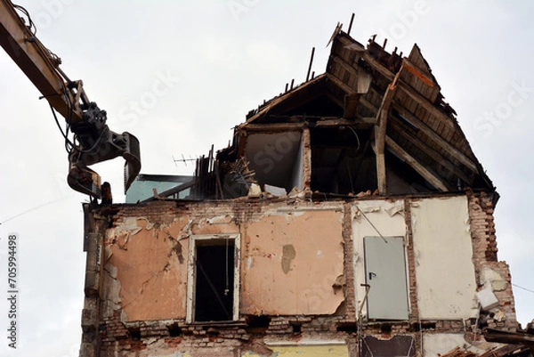 Fototapeta Dismantling a building on a city street with an excavator. Reconstruction and renovation of cities