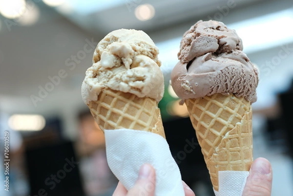 Fototapeta Two servings of ice cream cone on background of Mall, two girls clinking together with a brown, like glasses, game of communication, Friendship, eating delicious dessert. chocolate ice cream