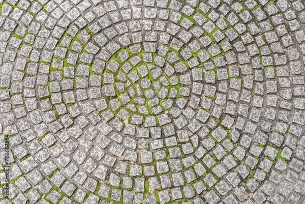 Fototapeta Patio pavers circle design overhead view.
Cut square stones in weathered floor with green moss.