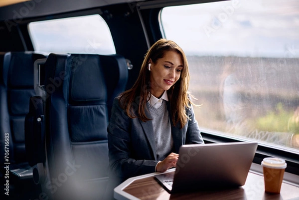 Fototapeta Smiling businesswoman works on laptop while commuting by train.