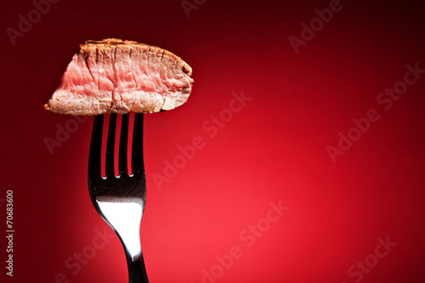 Fototapeta Piece of a grilled steak on a fork isolated on red