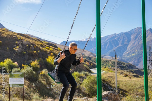 Fototapeta Man relaxing on a swing while enjoying the surrounding mountains and vast landscape